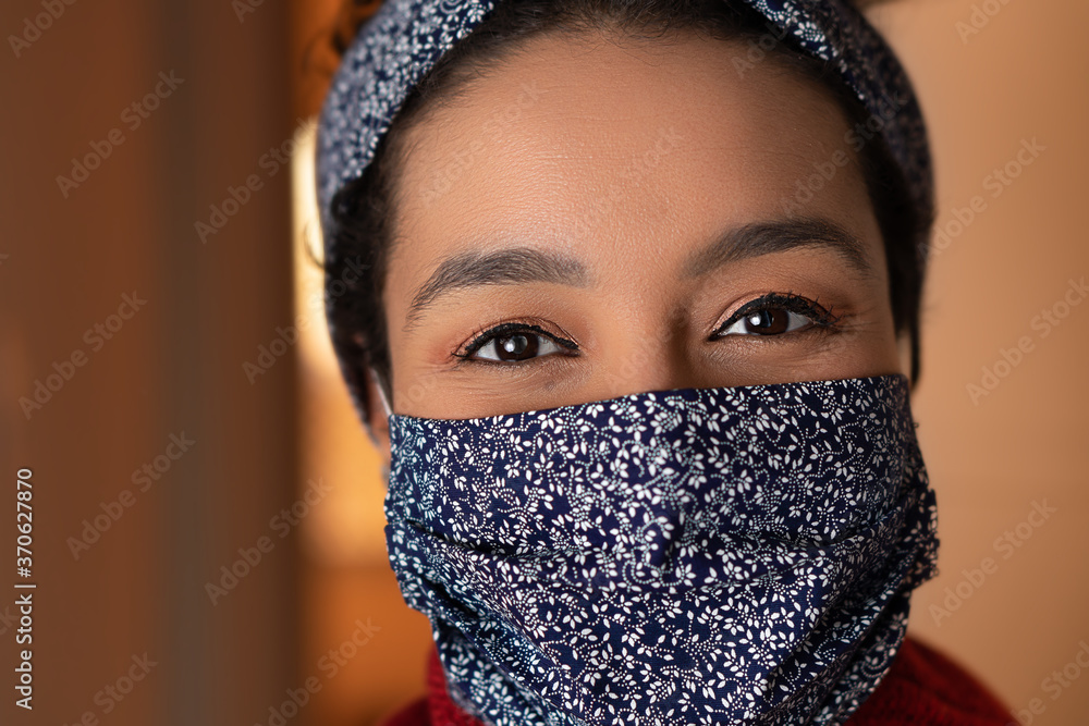 Close up of positive black woman with blue mask looking at camera. At apartment door entrance. Individuality, style, identity, Coronavirus or Covid-19 quarantine concept. Close up of positive black woman with blue mask looking at camera. At apartment door entrance. Individuality, style, identity, Coronavirus or Covid-19 quarantine concept.