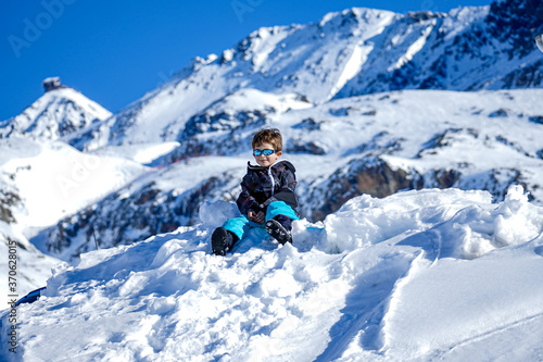 Young Boy Sitting On The Snow Mountain. Winter time