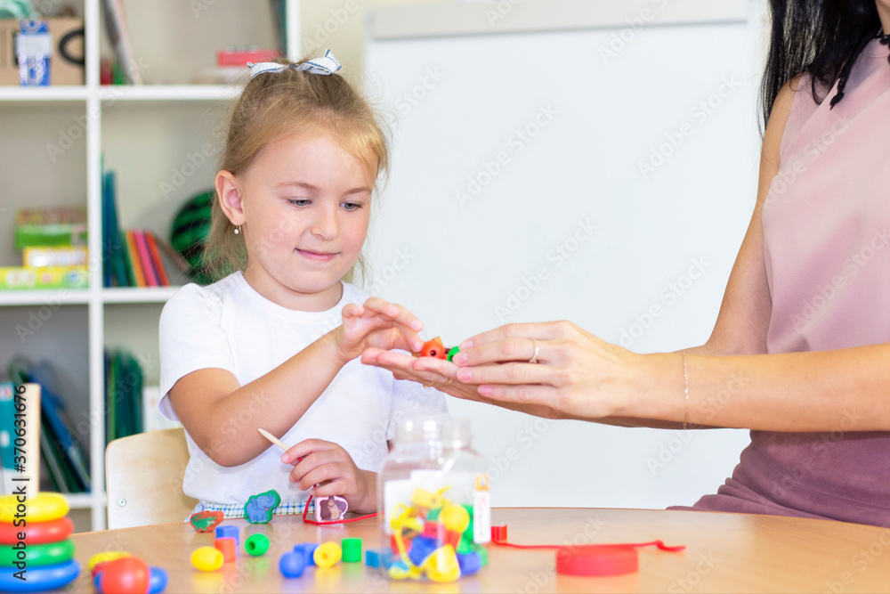 Fototapeta premium developmental and speech therapy classes with a child-girl. Speech therapy exercises and games with beads. The girl has beads in her hands