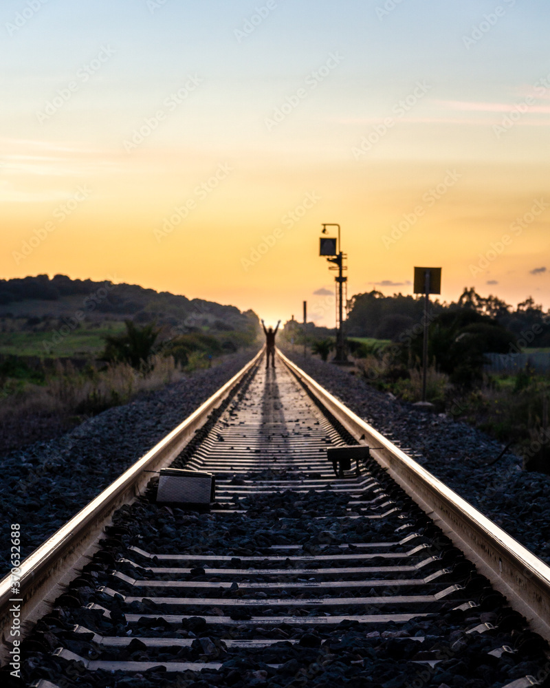 Man Standing on Railroad Tracks at Sunset