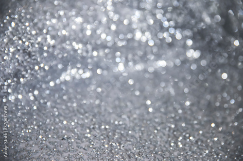 Macro photography with defocused shimmering glitter fabric in silver shade for Christmas greeting card. Sparkle background with shiny blur effect. Festive abstract glitter bokeh background.