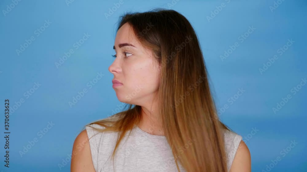 Sad woman in gray t-shirt looks around raises hands cannot make choice on blue background with copy space. 4K slow motion footage Sad woman in gray t-shirt looks around raises hands cannot make choice on blue background with copy space. 4K slow motion footage