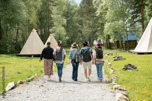 Rear view of young people with satchels arrived at campsite walking along path at festival campsite