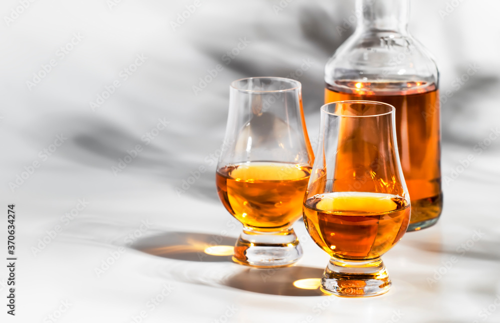 Scotch Whiskey without ice in glasses and bottle, white background with hard light, shadows and sun glare, copy space