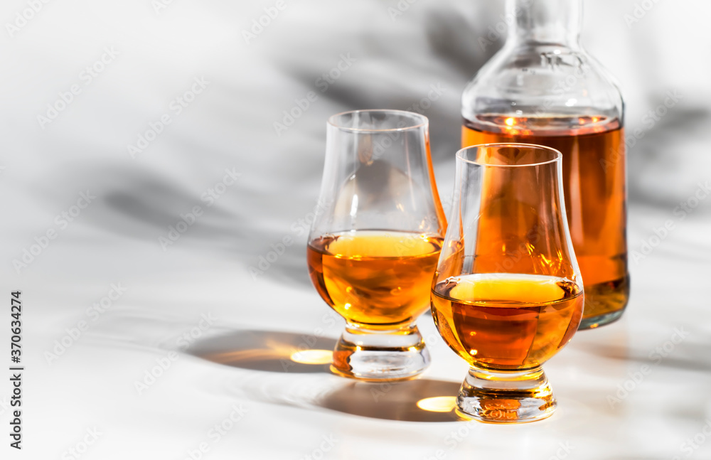 Scotch Whiskey without ice in glasses and bottle, white background with hard light, shadows and sun glare, copy space Scotch Whiskey without ice in glasses and bottle, white background with hard light, shadows and sun glare, copy space
