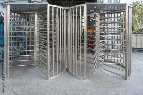 Protected entrance gate secured turnstiles outdoors. Steel revolving turnstiles at the entrance of production or metro station. Closeup of steel revolving security turnstile on the street