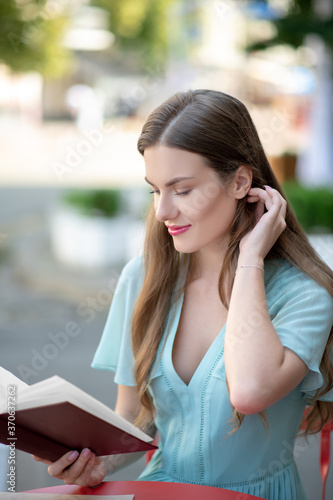 Charming brown-haired female, reading book, stroking her hair