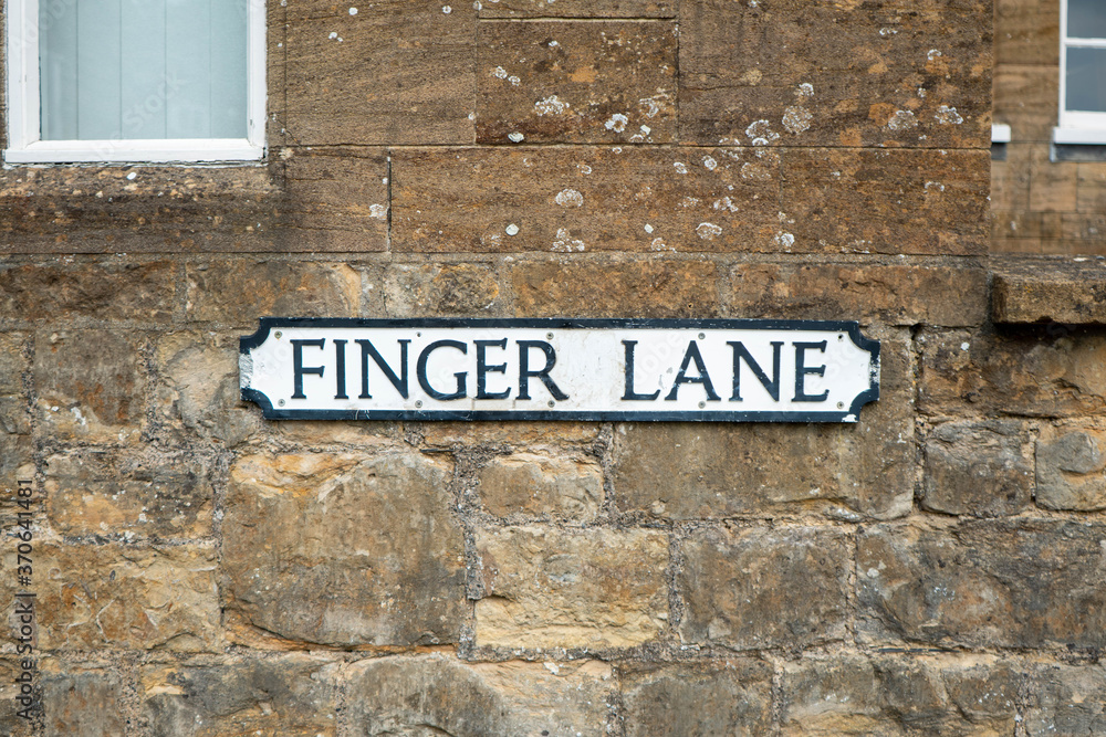 Fototapeta A street sign in the centre of the frame set against a brick stone wall. The road sign says Finger Lane in traditional black on white UK town sign style