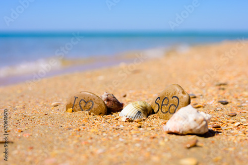 Pebbles with the inscription I love the sea on the beach by the sea. Several shells lie near the pebbles. Sea travel concept.