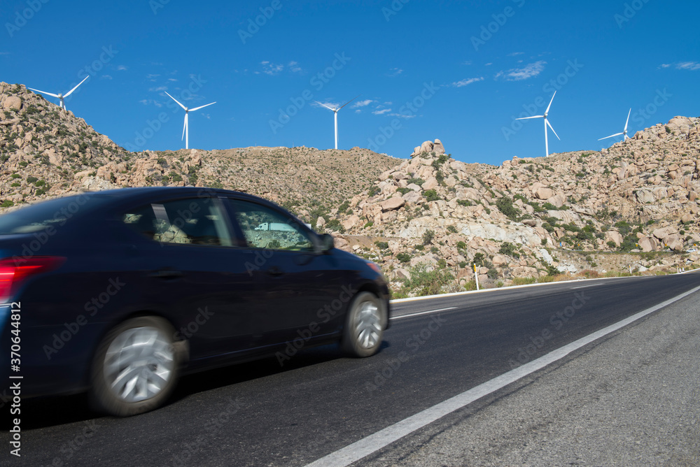Vehicle or car in motion, motion blur on the road from Mexicali to Tijuana, in the state of Baja California, MEXICO, with wind electric generators on top of the rocky mountains, in a sunny blue sky.