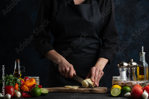 Chef prepares a dish of slicing potatoes, on a background with fresh vegetables, cookery and a book of recipes