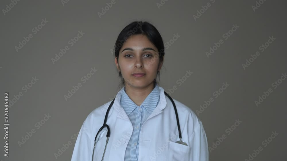 Confident smiling young indian female doctor wear white medical coat, stethoscope look at camera standing arms crossed on background. Indian health care professional medic gp physician portrait. Confident smiling young indian female doctor wear white medical coat, stethoscope look at camera standing arms crossed on background. Indian health care professional medic gp physician portrait.