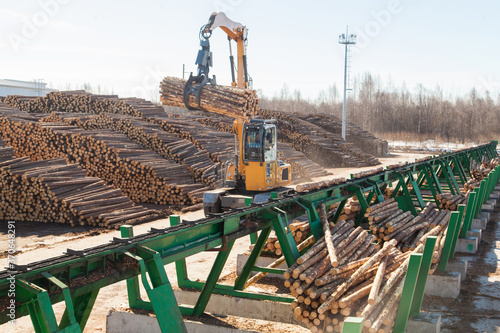 An industrial loader loads logs into a conveyor at a sawmill
