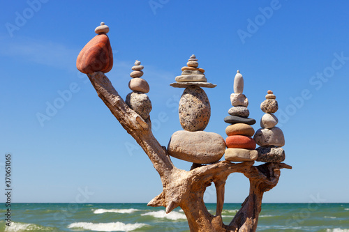 stack of multicolored balanced stones on an old wooden snags, on a blue sky and sea background