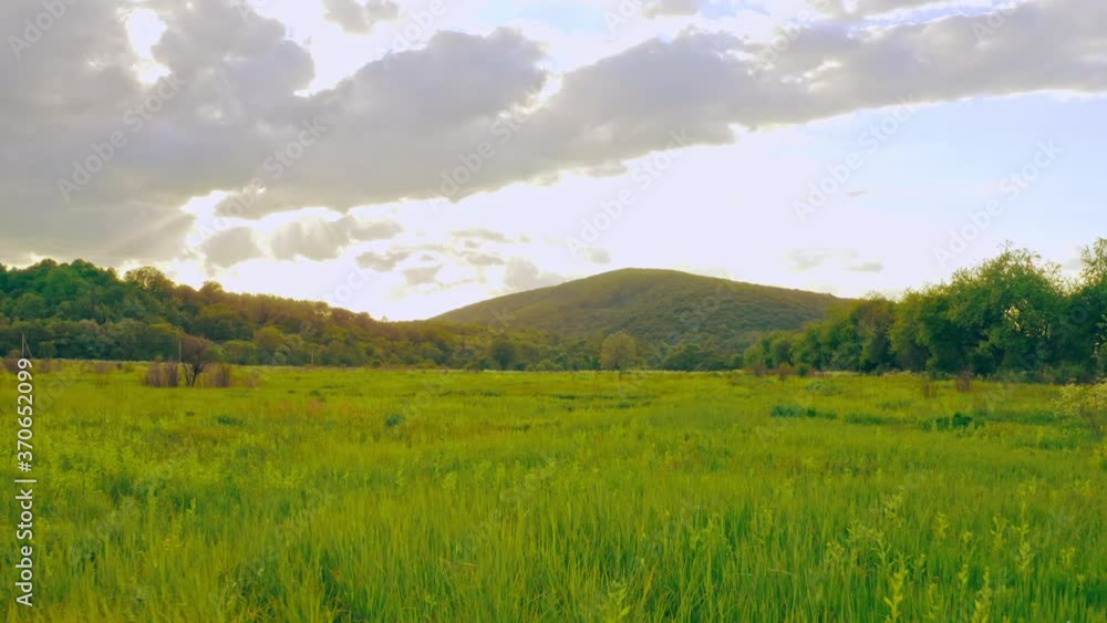 drone flies above meadow with green grass blue sky with sun rays through the clouds summer landscape with mountain on the background drone flies above meadow with green grass blue sky with sun rays through the clouds summer landscape with mountain on the background