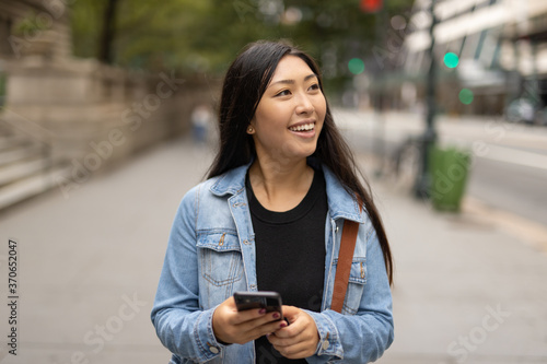 Young Asian woman walking street texting cellphone