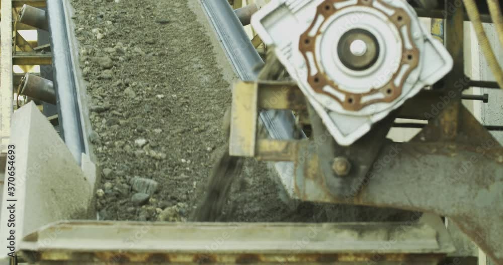 Raw building material, rocks, and earth transporting on the conveyor belt of stone crusher plant machine during the work process of separation, line production, close-up shot. Raw building material, rocks, and earth transporting on the conveyor belt of stone crusher plant machine during the work process of separation, line production, close-up shot.
