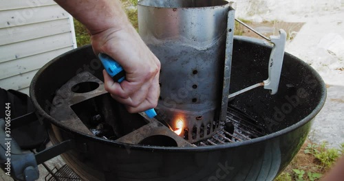 Man with long lighter ignites paper in a charcoal barbecue chimney fire starter