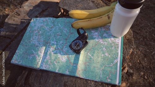 Close up things for tourism travel for eco tourism in nature forest. Paper map, compass and snack food bottle flask with water and bananas fruit on stumped hemp tree photo