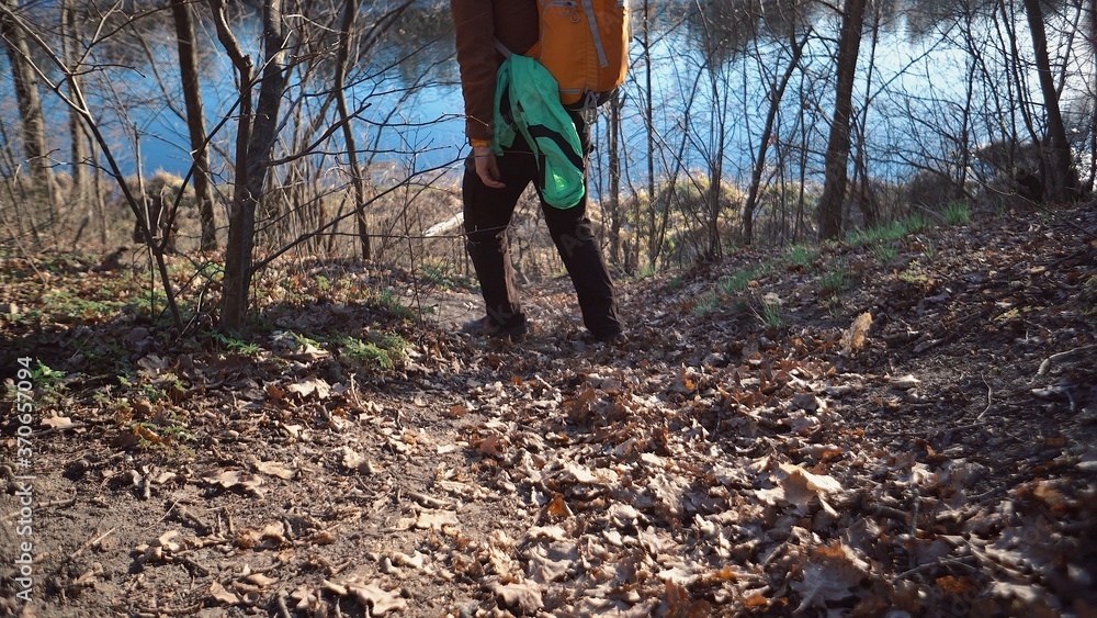 The theme of tourism and travel in nature. Caucasian man with a backpack hike down a hill covered with foliage and trees to the lake reservoir. Active leisure in the forest sunny weather The theme of tourism and travel in nature. Caucasian man with a backpack hike down a hill covered with foliage and trees to the lake reservoir. Active leisure in the forest sunny weather