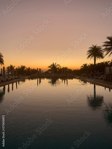Reflective lounge pool lined with palm trees at sunset © Michael