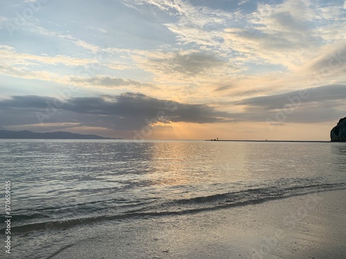 Landscape view of calm beach waters under cloudy sunset rays