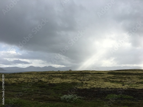 Landscape view of cloudy sun beams over rural mountain valley field 