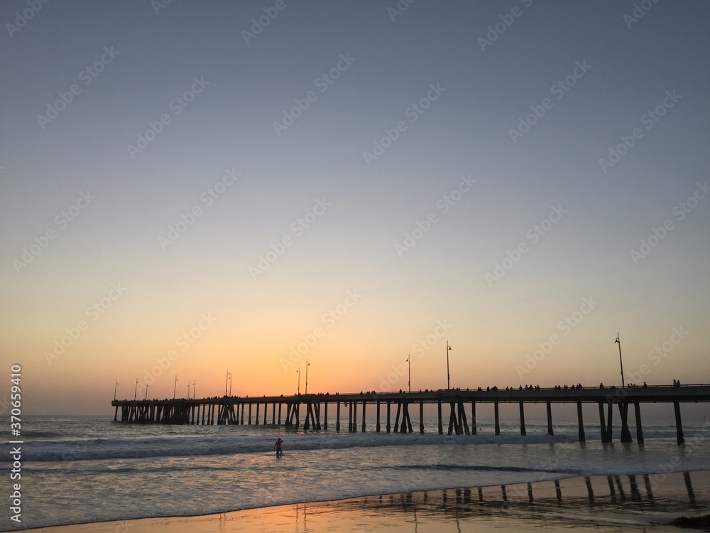 Landscape view of pier over sandy beach shore at sunset