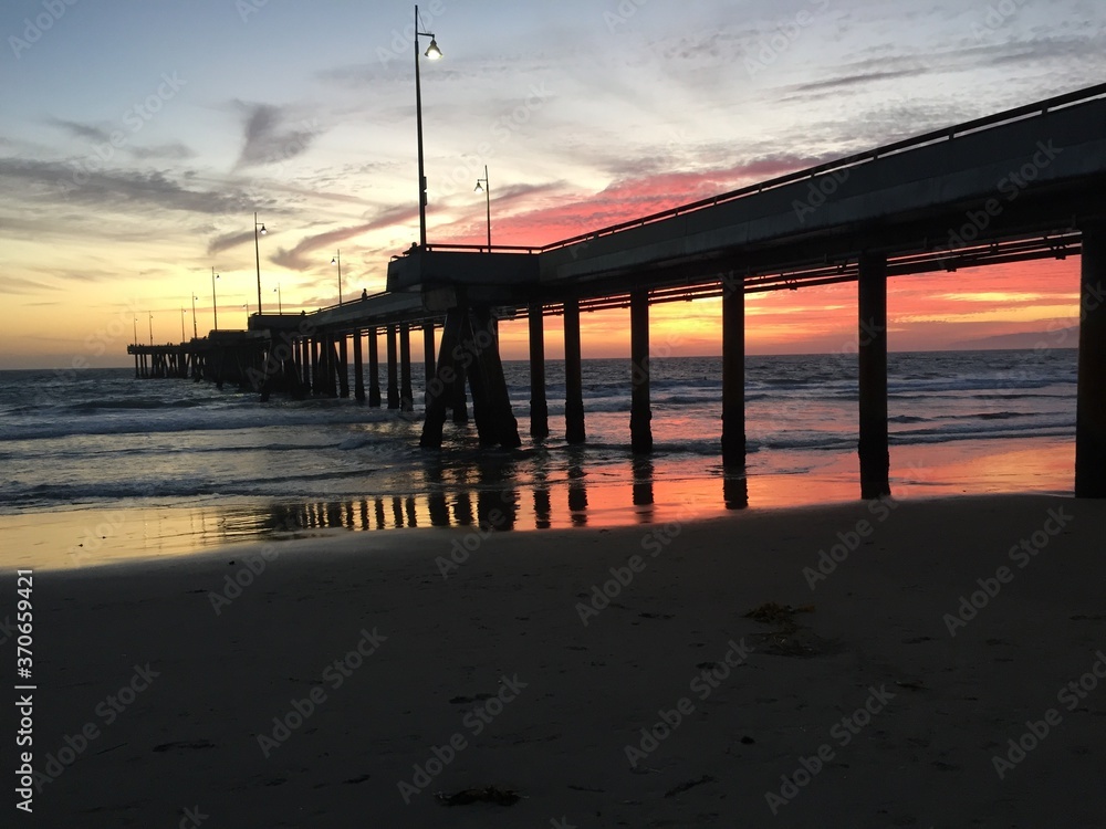 Fototapeta premium Landscape view of pier over sandy beach shore at sunset