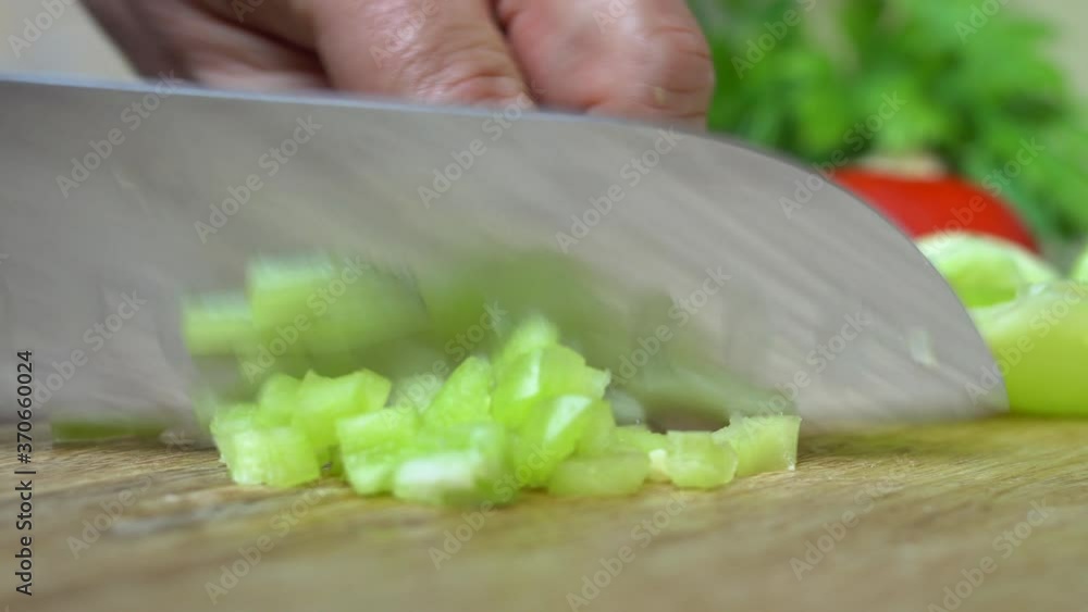Dicing green bell pepper on a wooden cutting board..Pan right. Placing small pieces of sweet pepper on a plate with a kitchen knife..Close up. Shallow depth of field, selective focus. Dicing green bell pepper on a wooden cutting board..Pan right. Placing small pieces of sweet pepper on a plate with a kitchen knife..Close up. Shallow depth of field, selective focus.