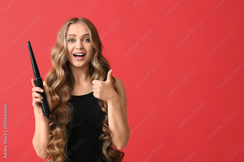 Beautiful young woman with curling iron for hair showing thumb-up against color background Beautiful young woman with curling iron for hair showing thumb-up against color background