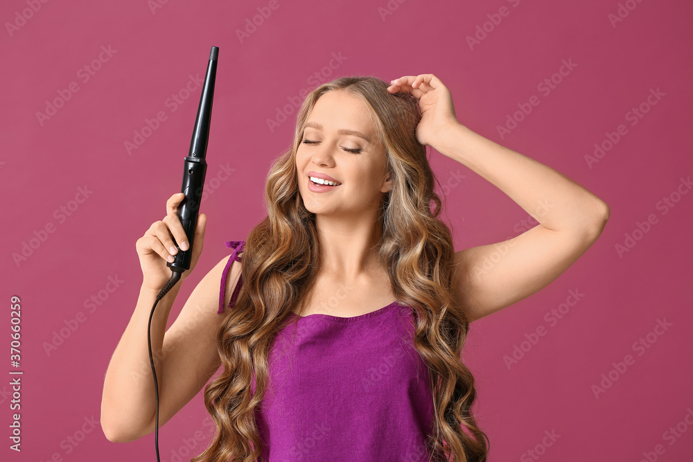Beautiful young woman with curling iron for hair against color background Beautiful young woman with curling iron for hair against color background