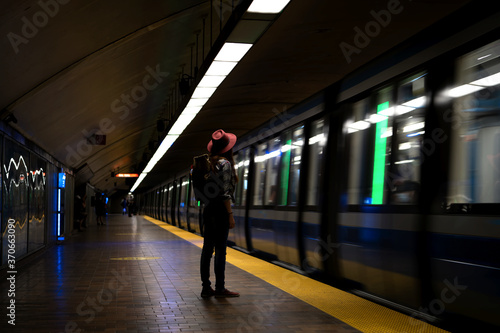 Redhead girl waiting for the train standing alone in a subway station wearing a red hat and a travel backpack