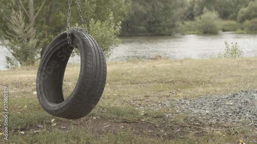 Lonely tire swing hangs on chain along riverbank, slow motion photo
