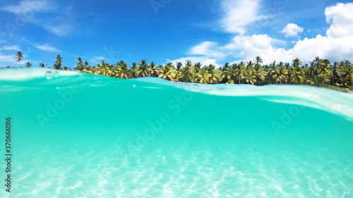 Half in half out crystal turquoise water of calm ocean surface and the idyllic beach with palm trees and blue sky. Vacations on a paradise tropical island. 