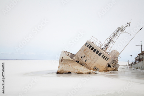 Abandoned white ship frozen in ice near lighthouse