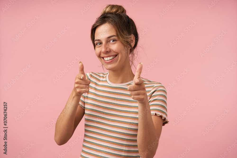 Indoor shot of young beautiful brown haired woman with natural makeup smiling happily while showing with raised hands at camera, isolated over pink background Indoor shot of young beautiful brown haired woman with natural makeup smiling happily while showing with raised hands at camera, isolated over pink background