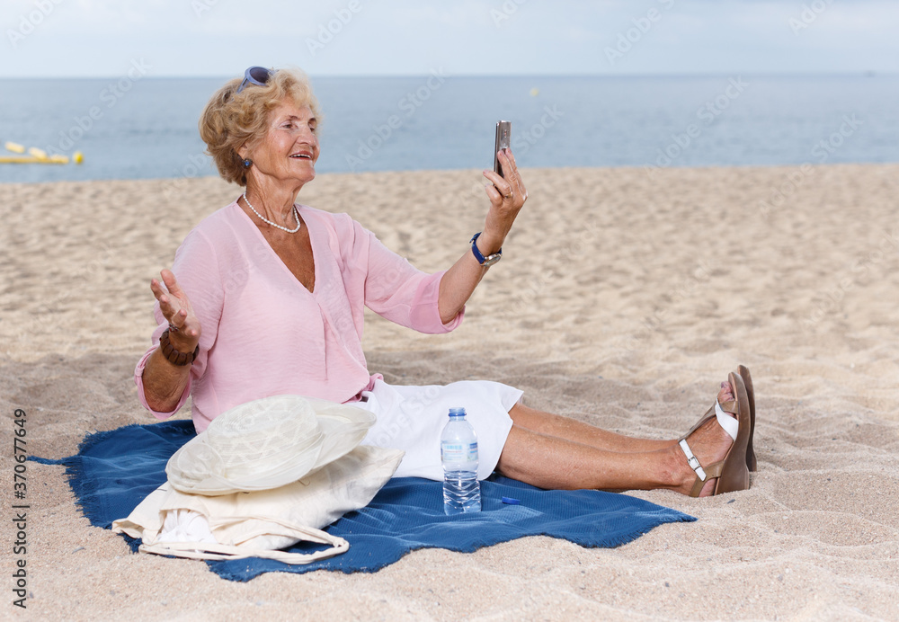 Smiling senior lady relaxing on beach walk and making selfie