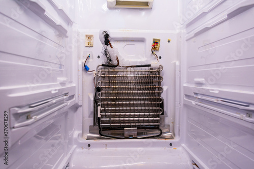 Refrigerator repair. Freezer compartment back panel removed. Evaporator coils with a frozen thermostat.