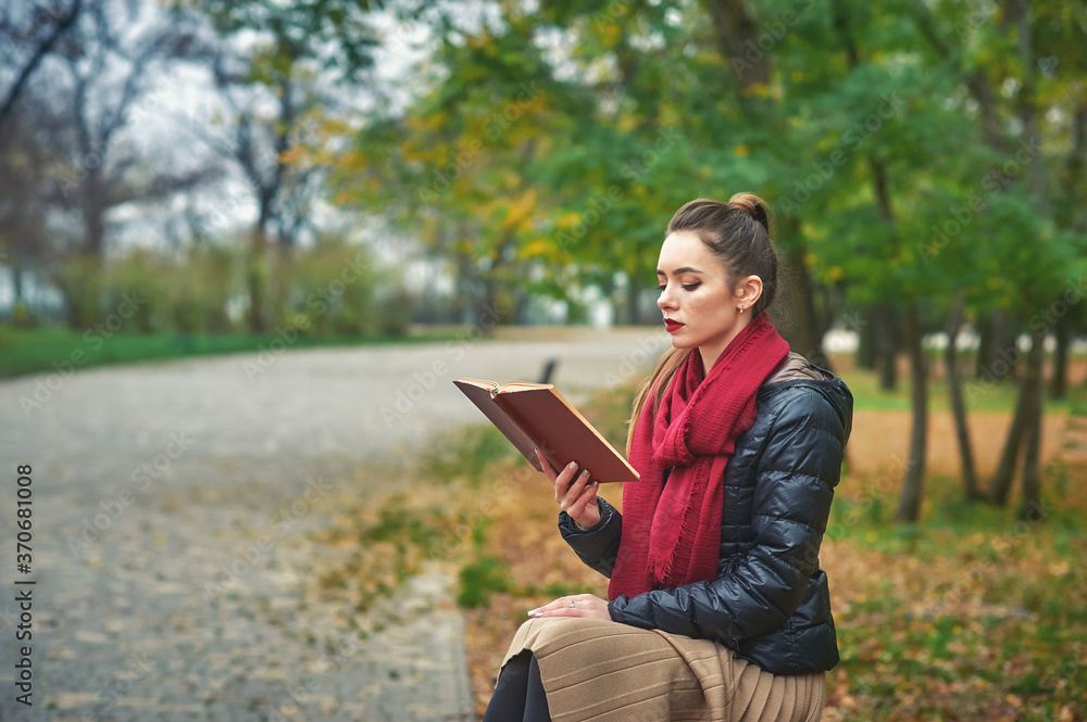 Obraz premium Portrait of a young woman with a book in an autumn Park . Reading fiction in the open air