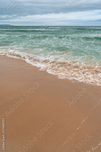Turquoise sea with waves and sea foam, sandy beach, cloudy sky
