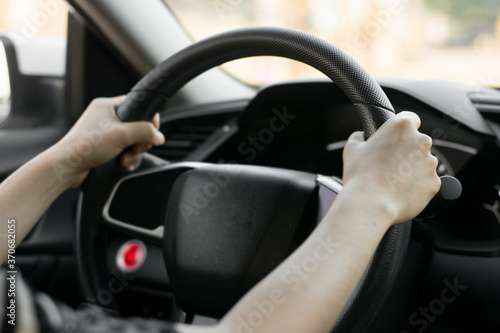 Female hands on the steering wheel of a car while driving. Against the background, the windshield and road,Close-up of a woman's hand driving a car © sek_gt