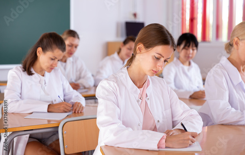 Medical students doing test in college, writing in notepads during lesson