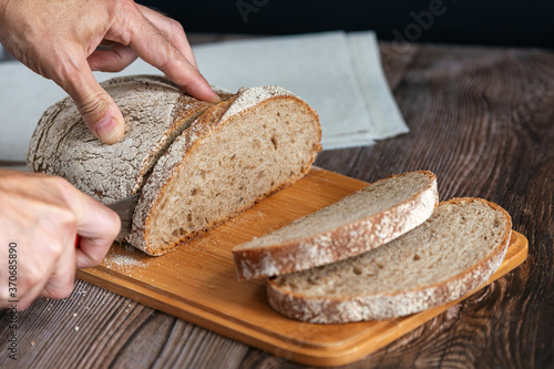Close up of hands cutting a slice of rey bread. Male hands cutting bread
