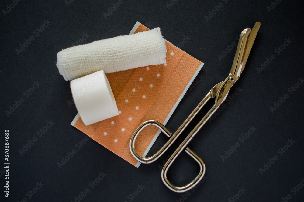 Obraz premium White bandage and medical scissors on black background