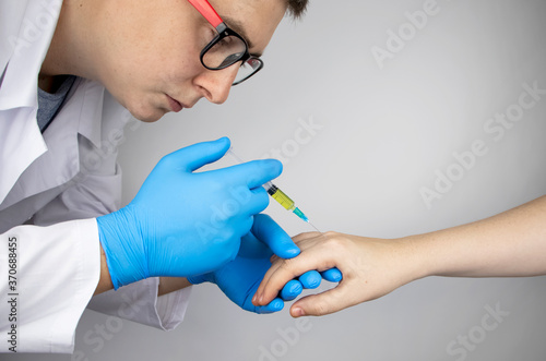Fototapeta Naklejka Na Ścianę i Meble -  Orthopedic surgeon gives an injection in the finger joint. Treatment of osteoarthritis with hormonal drugs or drugs based on hyaluronic acid. Help with diseases that damage the cartilage of the joint