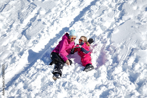 Happy family mother and girl daughter playing and laughing in winter snow. Little girl and her mother playing outdoors at sunny winter day. Active winter holidays concept.