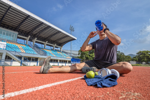 Fototapeta Naklejka Na Ścianę i Meble -  Young man stretching muscles before and after training and drink water from water bottle. Fitness and sport concept.