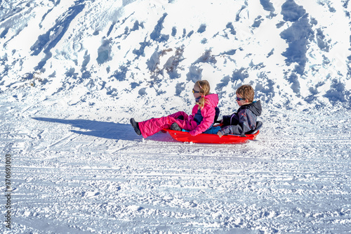Two joyful kids sledding down the hills on a winter day. Brother and sister