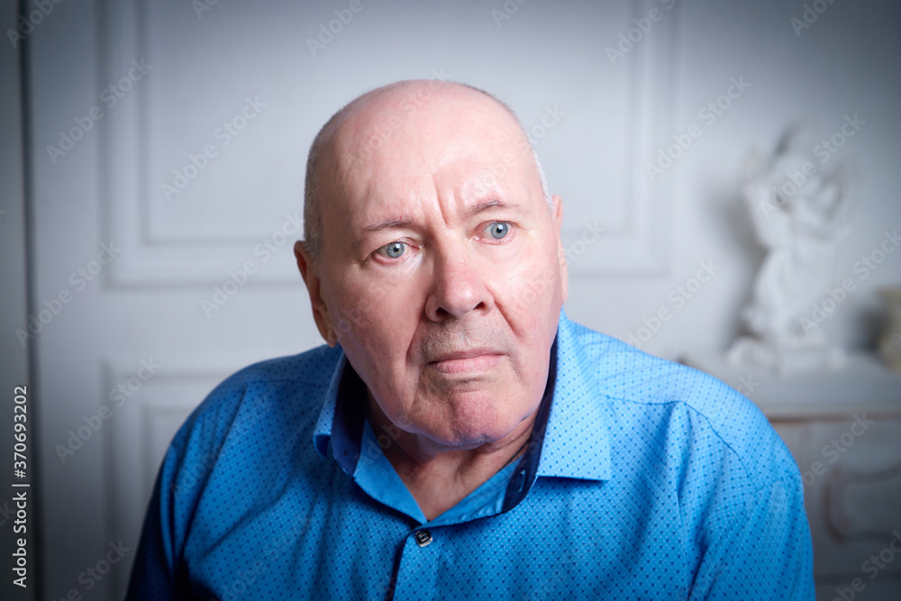 Portrait of an elderly bald man in a blue shirt in the room. A poor pensioner lives alone. Portrait of an elderly bald man in a blue shirt in the room. A poor pensioner lives alone.